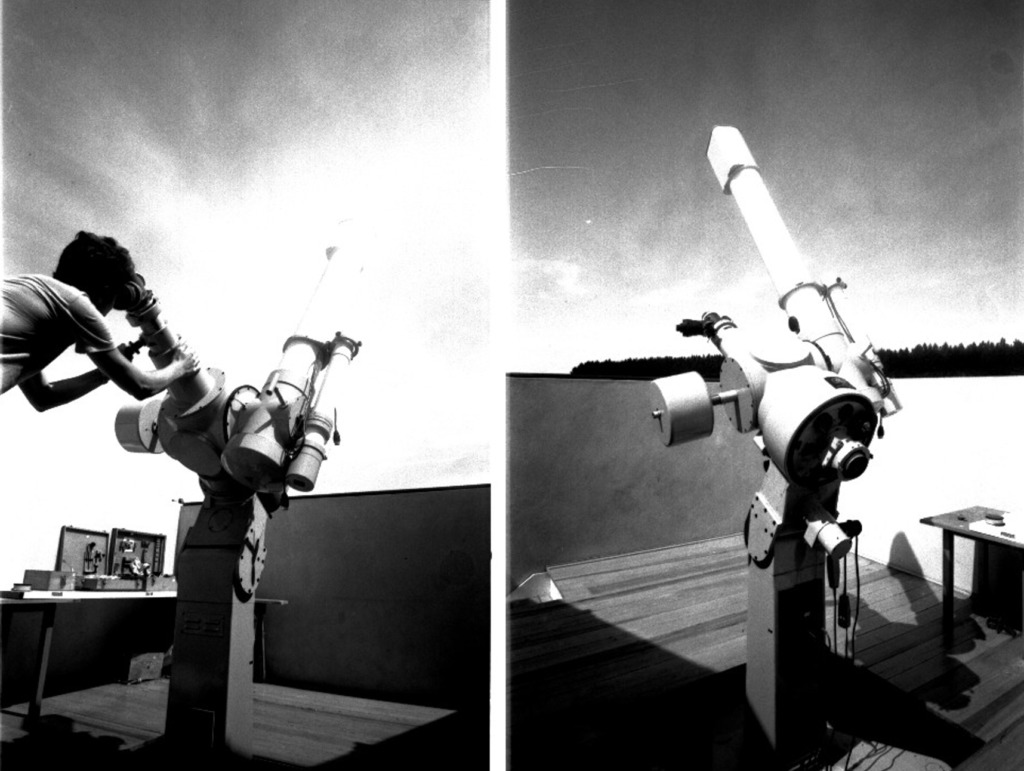 Audiodescrição da Imagem: Montagem horizontal de duas fotografias verticais, em preto e branco, postas uma ao lado da outra, de um homem que olha o céu através de um telescópio, em ambiente externo. Na imagem à esquerda, em um terraço, fixado no chão, o Telescópio Refrator Zeiss suportado por um grande e largo tripé de metal e engrenagens, levemente voltado para baixo, de aproximadamente um metro de altura. O telescópio é de um tom claro e composto por tubos em diversos tamanhos, e outras partes como: montura, buscador, tubo e ocular. Ao todo o equipamento tem por volta de três metros de altura, contando os tubos maiores e mais compridos, em torno de um metro de comprimento, sendo um deles do lado esquerdo e outro do lado direito. A imagem à esquerda foi tirada de frente e está mais clara no meio para a direita. Nela aparece parte do corpo de um homem de perfil direito, no alto, enquadrado da cintura para cima. Ele tem cabelo escuro volumoso e pele clara, veste camiseta clara, e apoia a cabeça no buscador para observar o céu pelo telescópio. É jovem, cerca de vinte anos, e segura com as duas mãos a montura grande do tubo que fica do lado esquerdo do instrumento. Ainda no lado esquerdo da imagem, mais afastada do telescópio, uma mesa retangular escura de pernas finas e sobre ela três caixas de madeira; uma delas fechada, e as outras duas, abertas e dentro se pode ver algumas ferramentas. E, ao fundo, do lado direito para o meio da fotografia, a parte de um muro horizontal escuro e piso amadeirado, sob um céu claro. Na imagem à direita, temos o telescópio registrado de perfil esquerdo, em que a fotografia foi registrada do canto esquerdo para o direito. Dessa vez, o aparelho aparece com o tripé de metal e engrenagens e a montura voltada para cima, direcionando o tubo maior para o céu. No canto inferior direito, parte de uma pequena mesa com alguns objetos em cima. As duas partes do muro horizontal escuro se encontram e formam um canto que contorna a imagem. O piso é amadeirado. Ao fundo, atrás do muro, topos de árvores alinhadas sob um céu claro. Audiodescritora Roteirista: Isabel Motta. Audiodescritora Consultora: Rubia Steffens