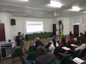 Fotografia horizontal e colorida de um homem falando ao microfone para um grupo de pessoas sentadas em um auditório